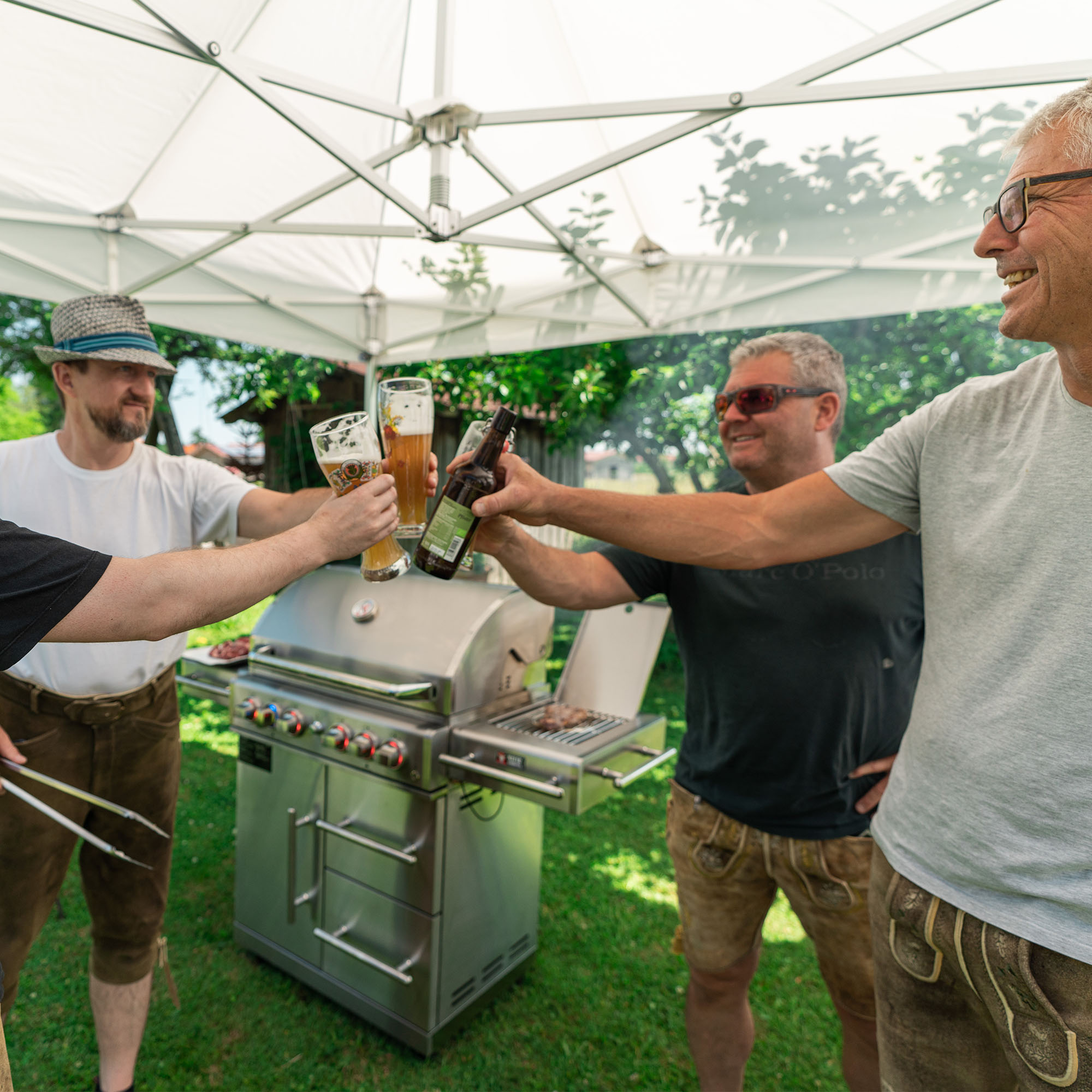 slider_image_c935deefa8544a9d8ad75d35e3120172 Gruppe von Menschen stößt mit Getränken an, während sie um einen Grill im Freien stehen