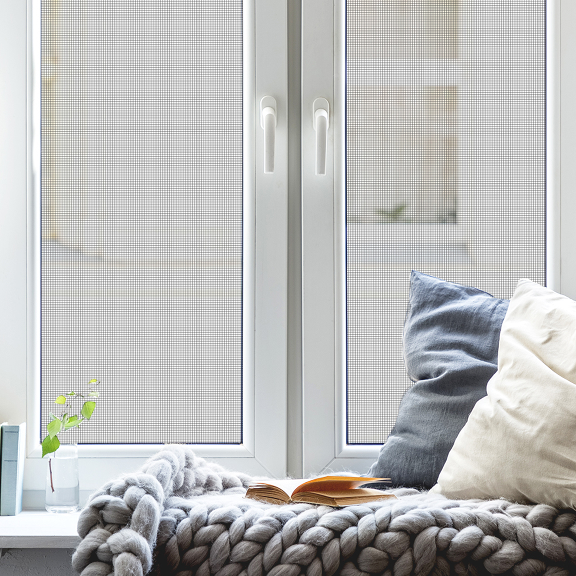 Fliegengitter an einem Fenster mit Kissen und Decke auf der Fensterbank