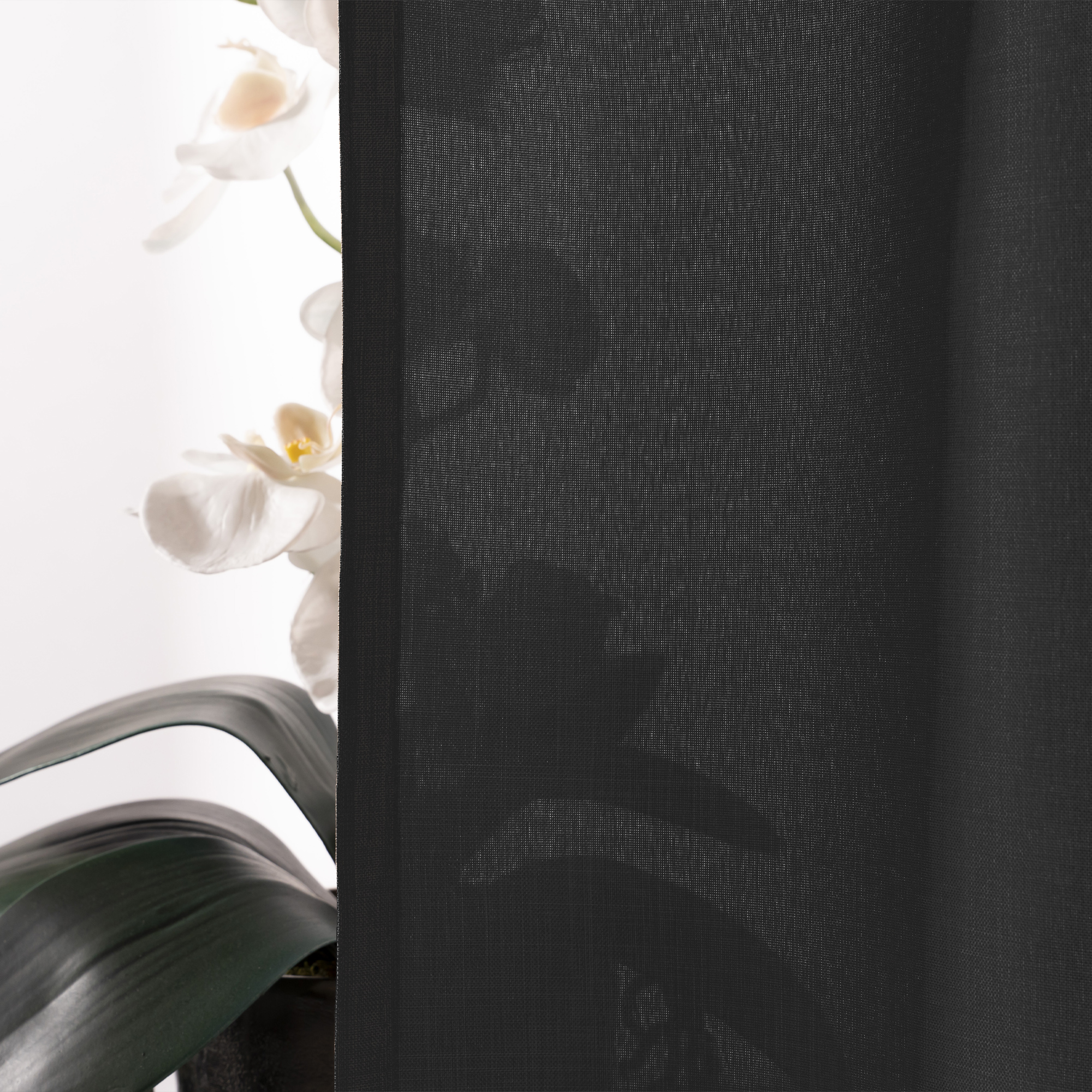 Vorhangdetail mit transparentem Stoff, im Hintergrund eine Pflanze mit Blüten