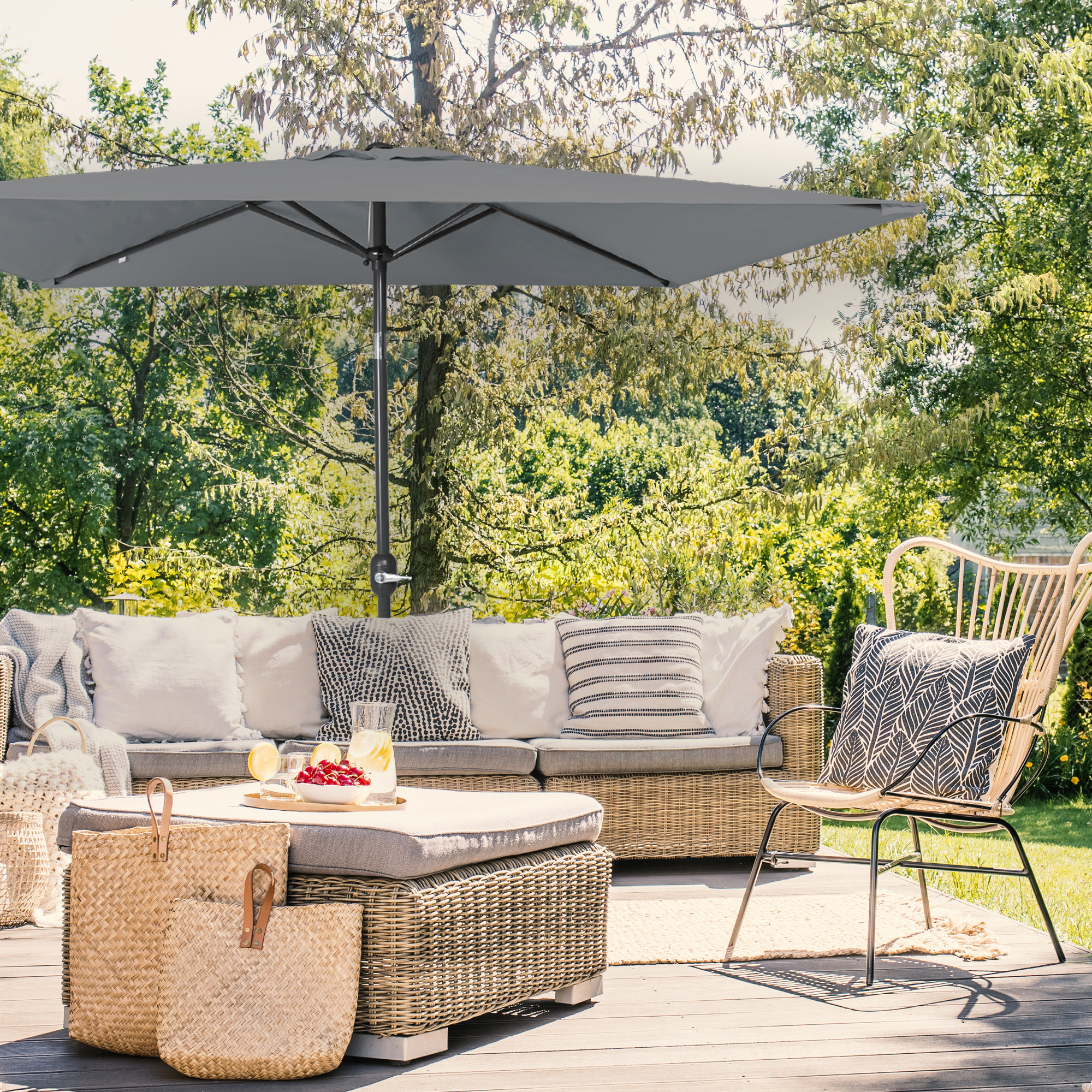 Kleiner, knickbarer Sonnenschirm über einer Terrasse mit Sitzmöbeln und Pflanzen im Hintergrund