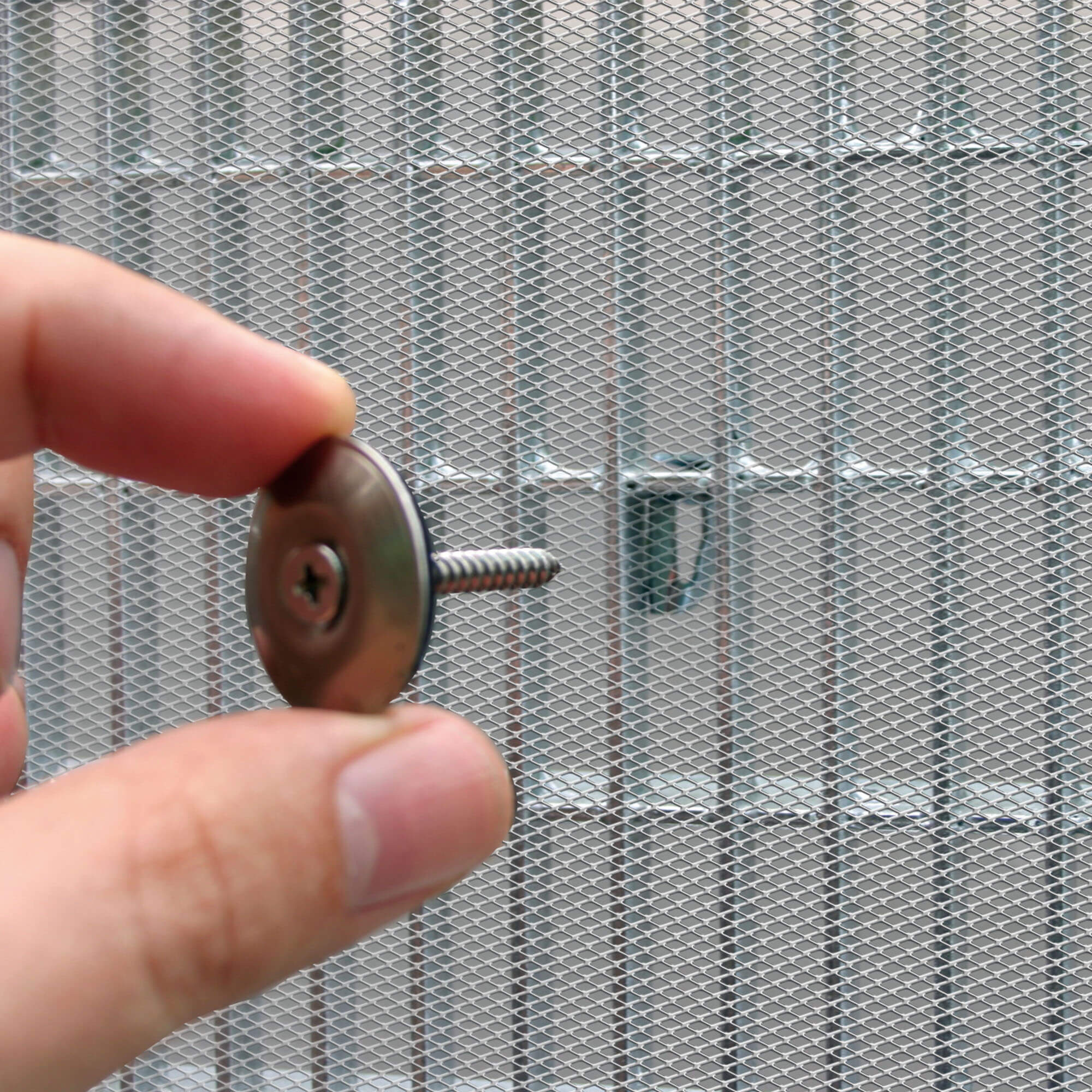 Hand hält Schraube vor Lichtschachtabdeckung mit Aluminiumrahmen und Gitterstruktur