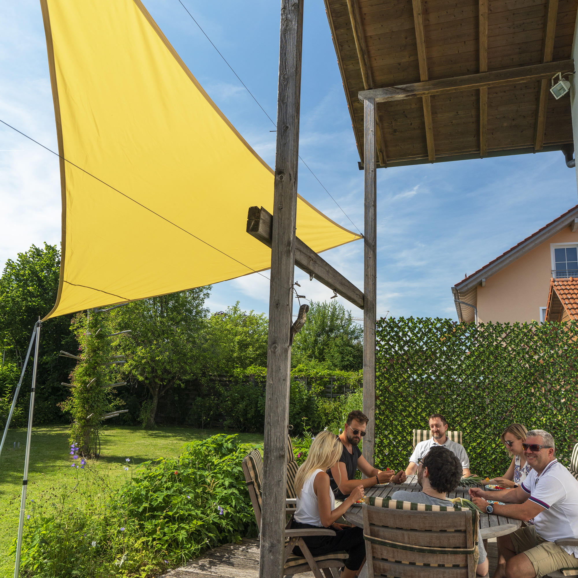 Personen sitzen unter einem Sonnensegel im Garten an einem Tisch