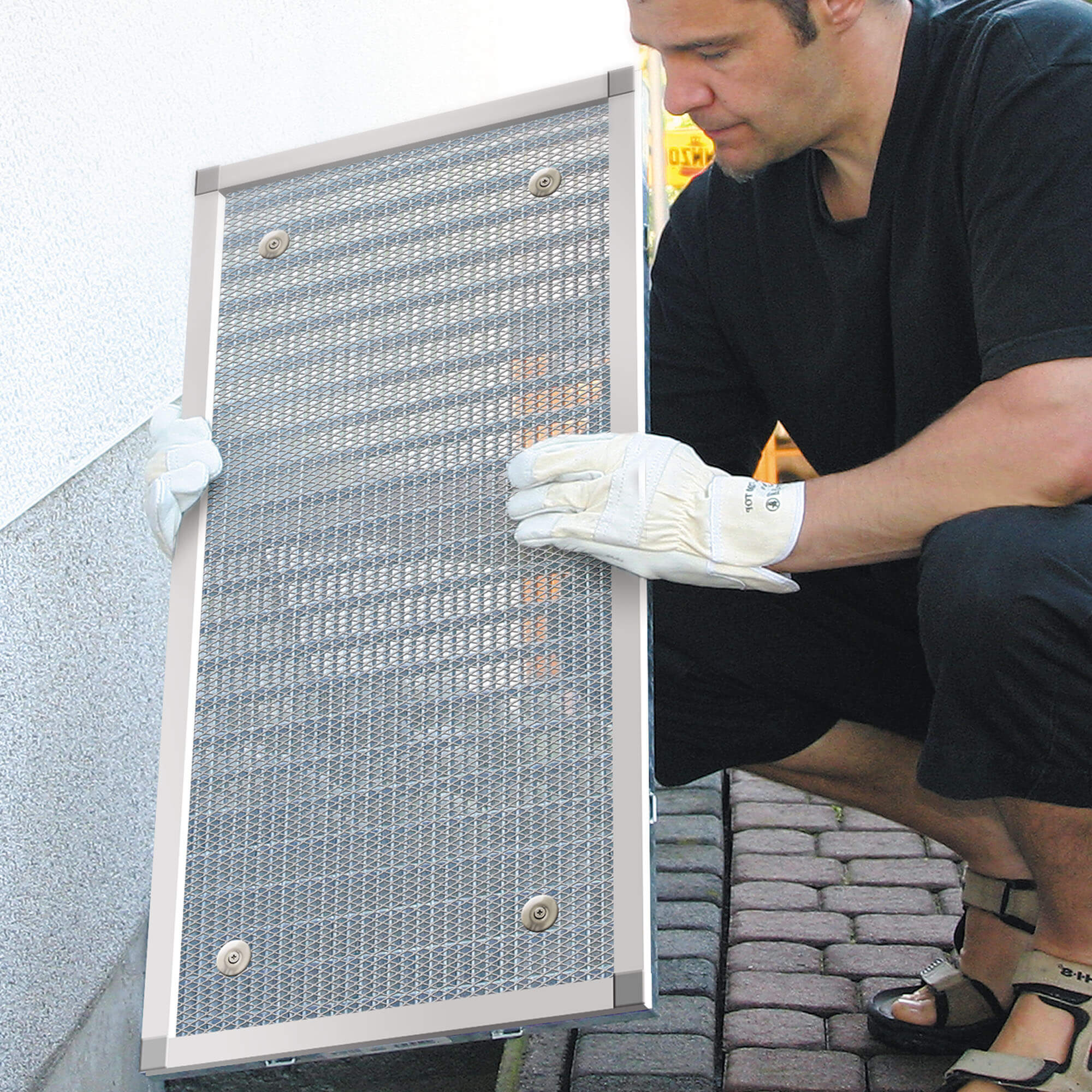 Person montiert Lichtschachtabdeckung mit Aluminiumrahmen an einer Wandöffnung