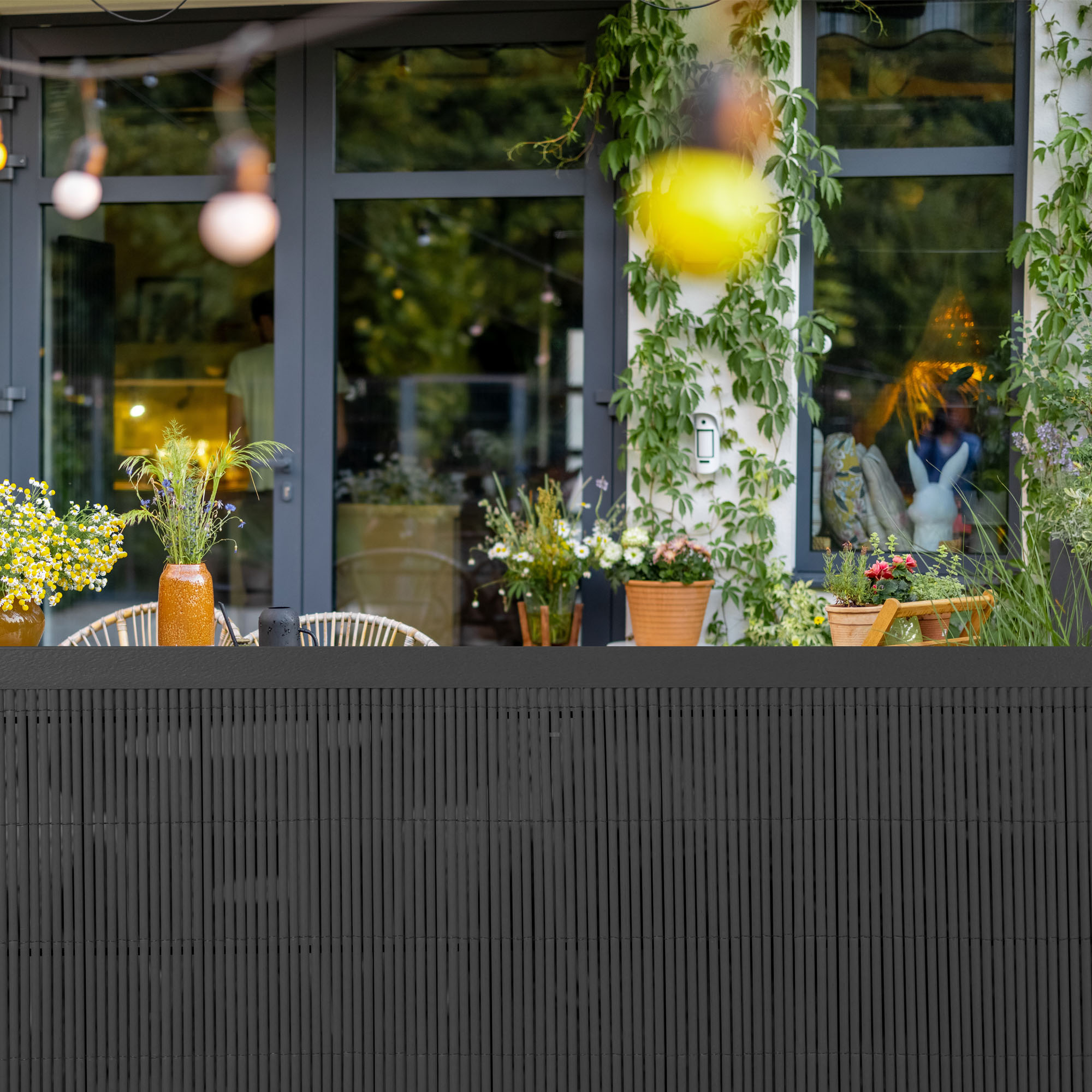 Abdeckprofil für Sichtschutzmatte vor Terrasse mit Pflanzen und Lichterkette