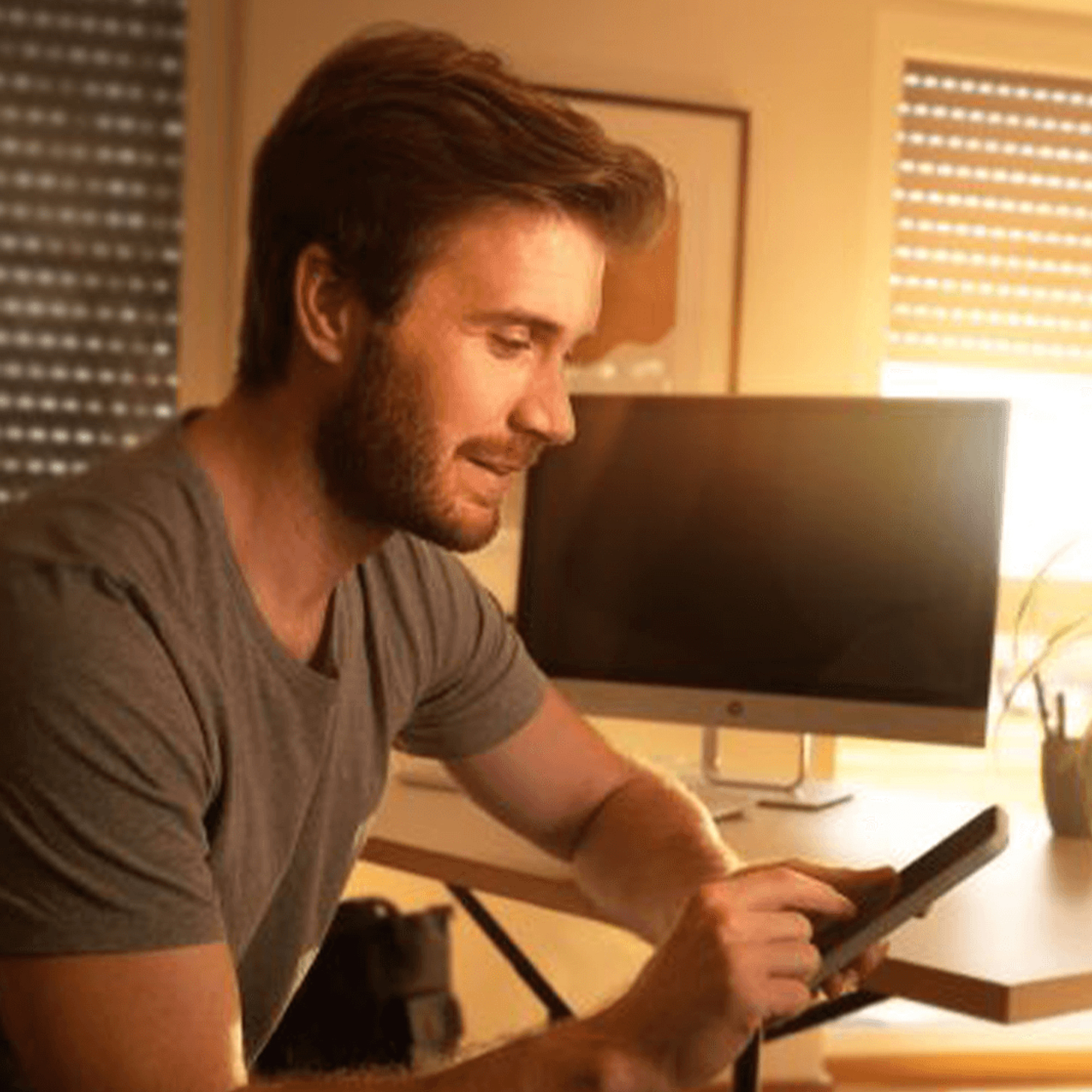 slider_image_0192756cef0373199a18511bb704afb4 Person sitzt an einem Schreibtisch und benutzt ein Tablet, im Hintergrund ein Monitor