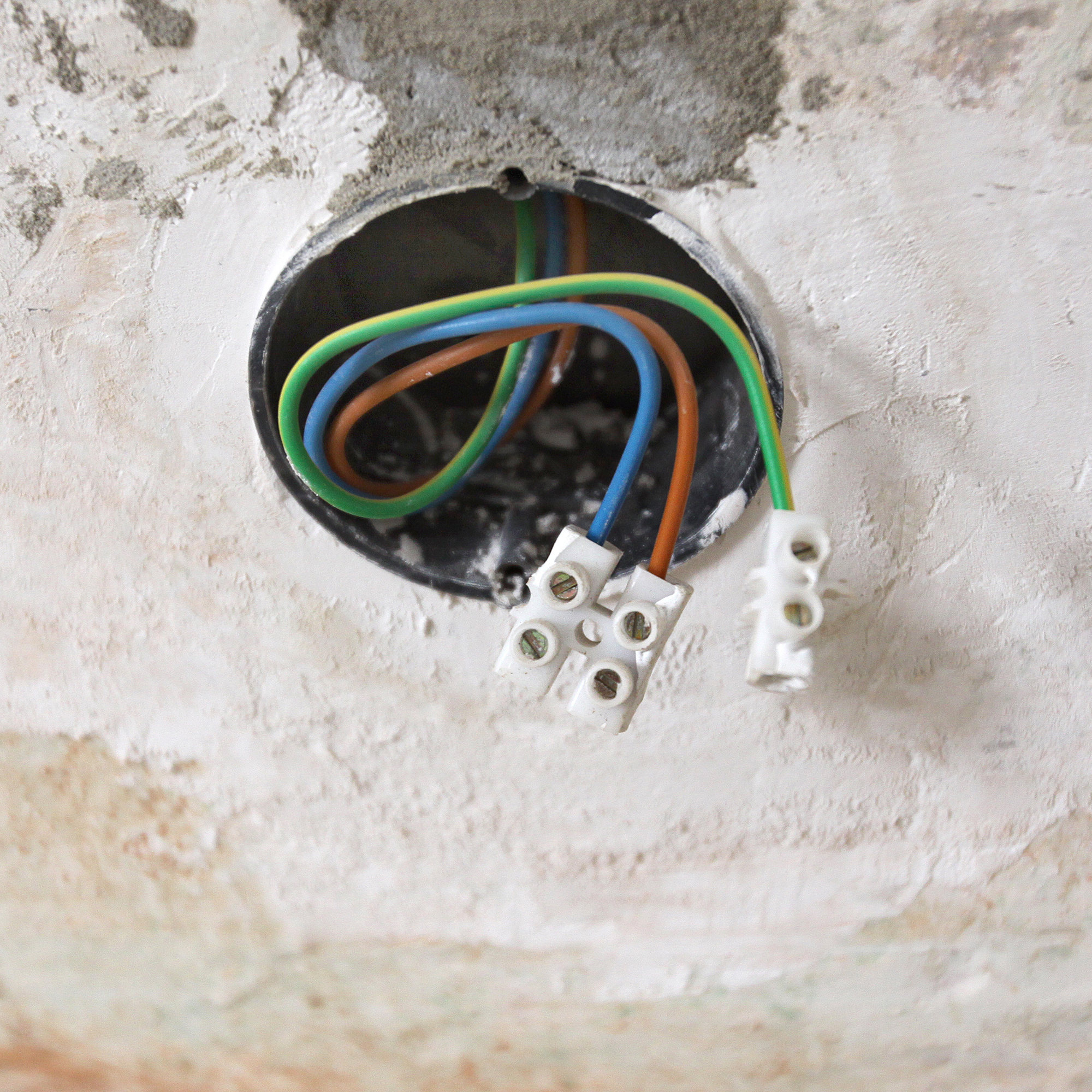 Unterputzdose mit herausragenden Kabeln und Lüsterklemmen in einer Wandöffnung