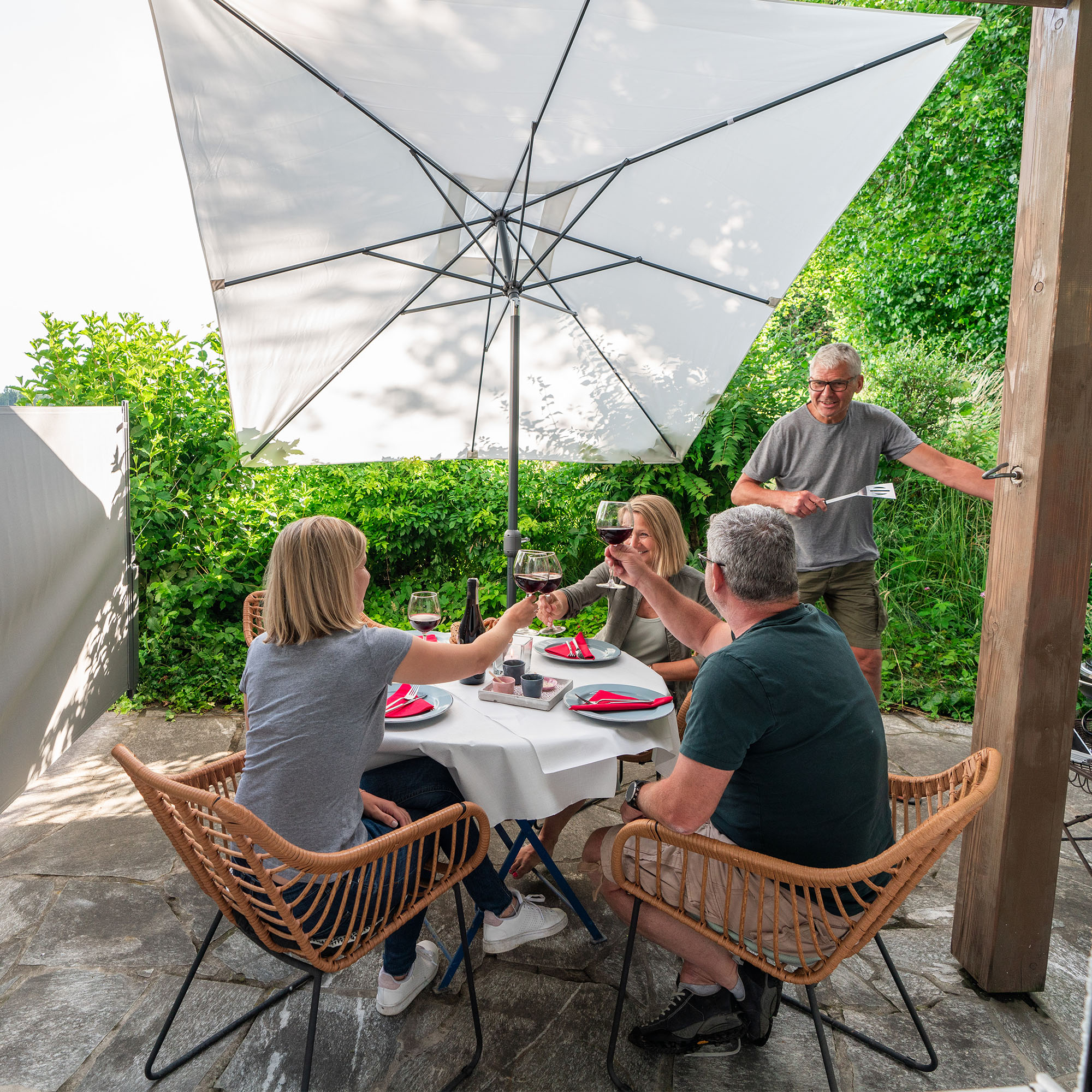 Personen sitzen unter einem Sonnenschirm an einem Tisch im Freien und stoßen mit Gläsern an