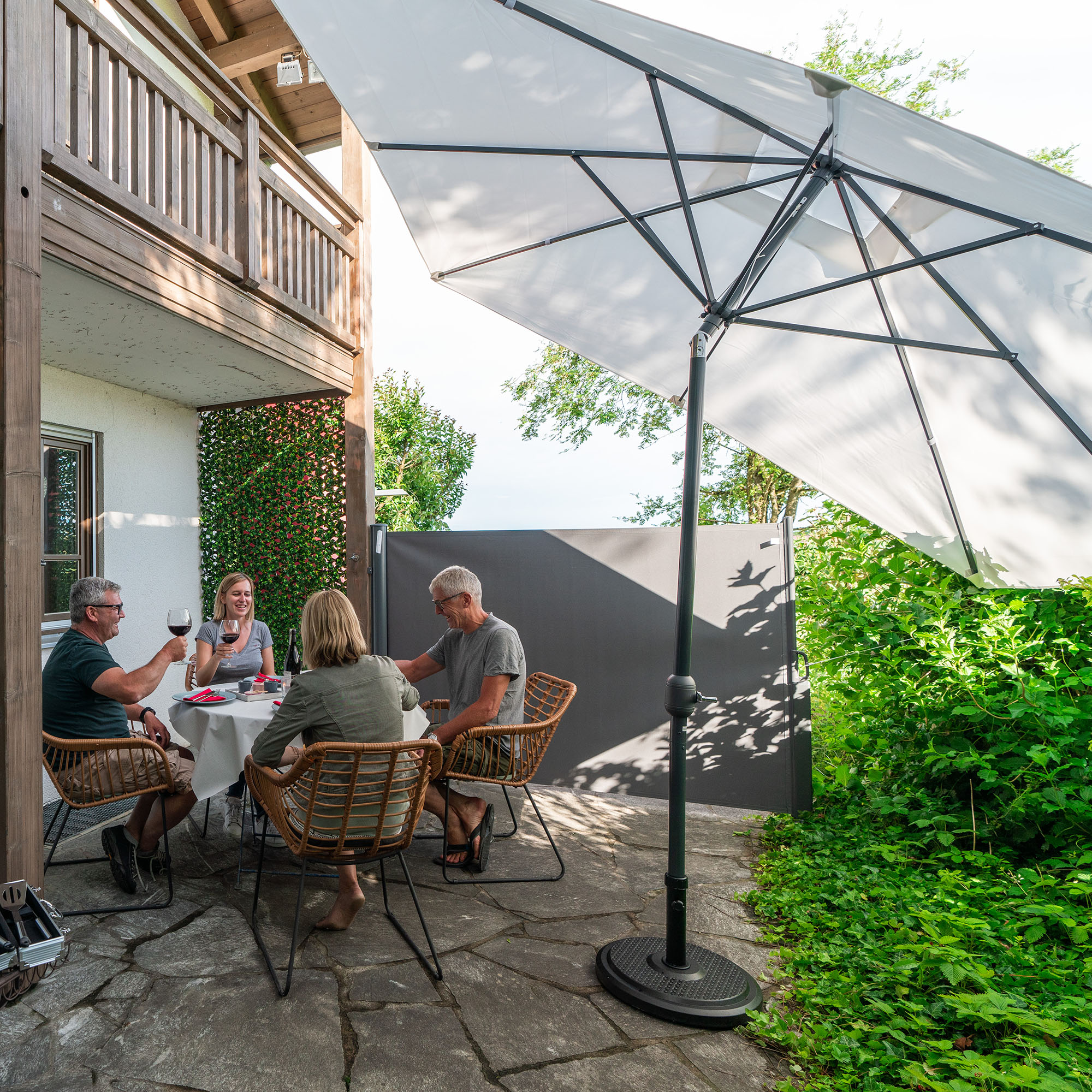 Sonnenschirm über Tisch mit vier Personen auf Terrasse, bietet Schatten und Schutz im Freien