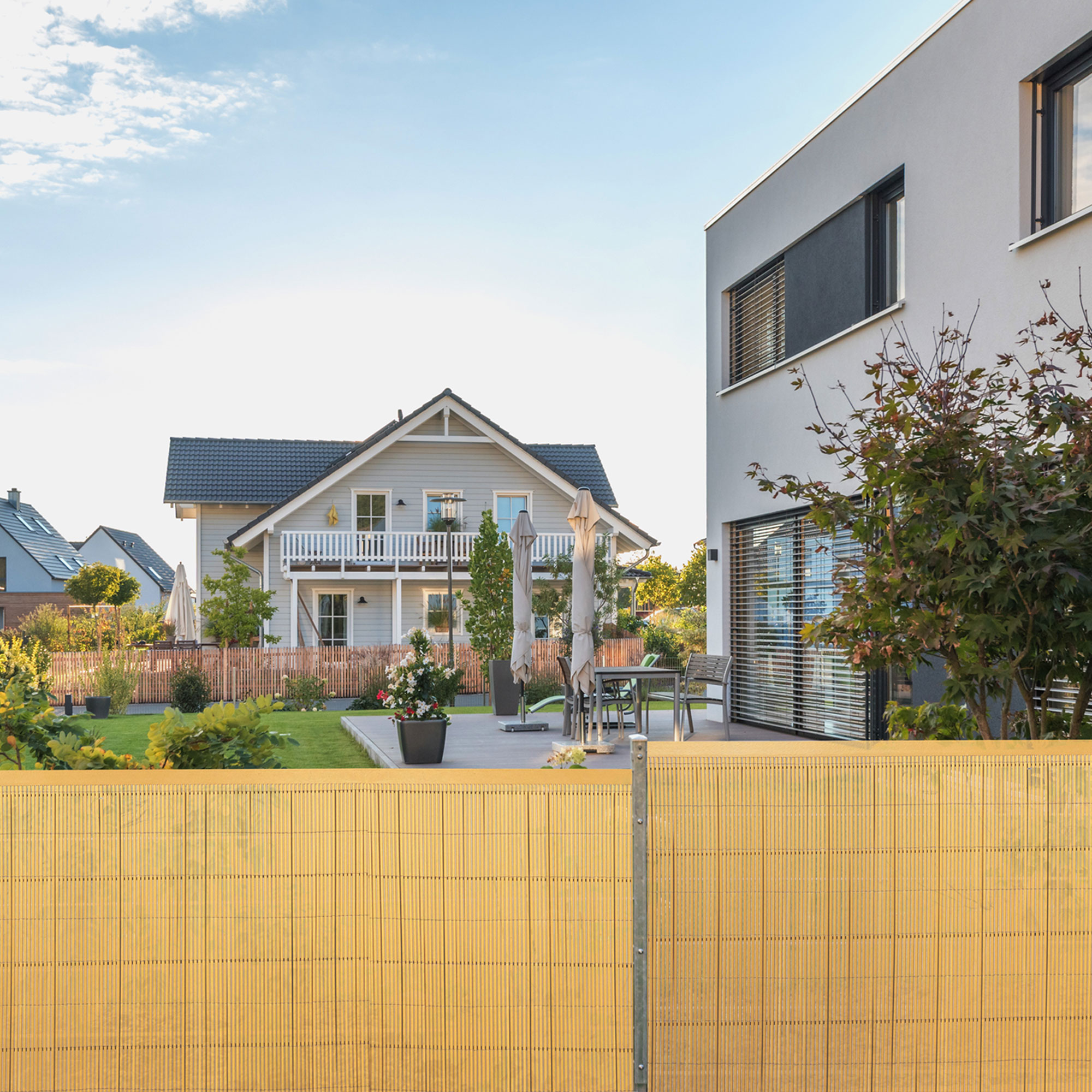 Bambuszaun vor einem Garten mit Haus im Hintergrund