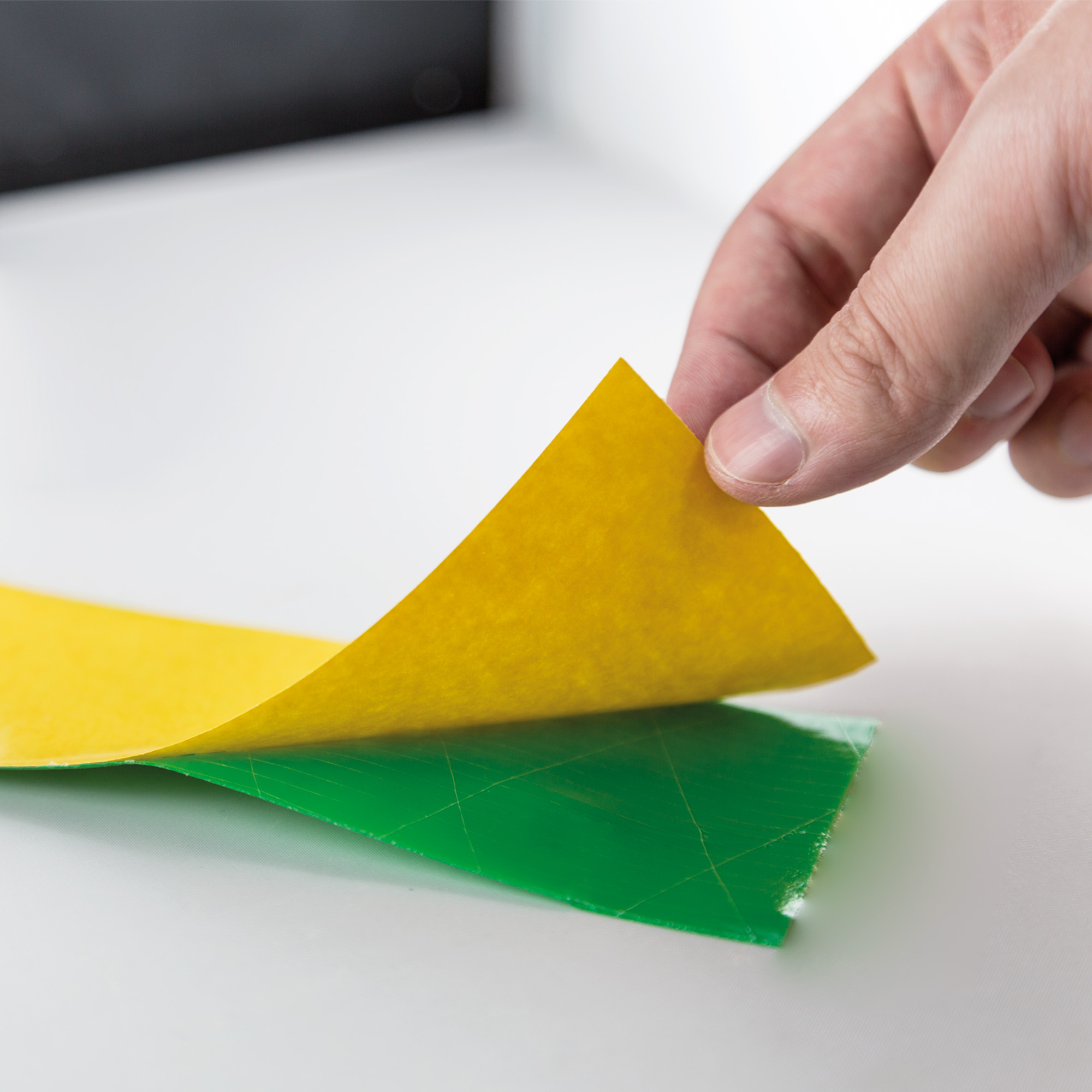 Hand zieht Schutzfolie von einem Klebeband ab, zeigt Schichten und Funktion des Produkts