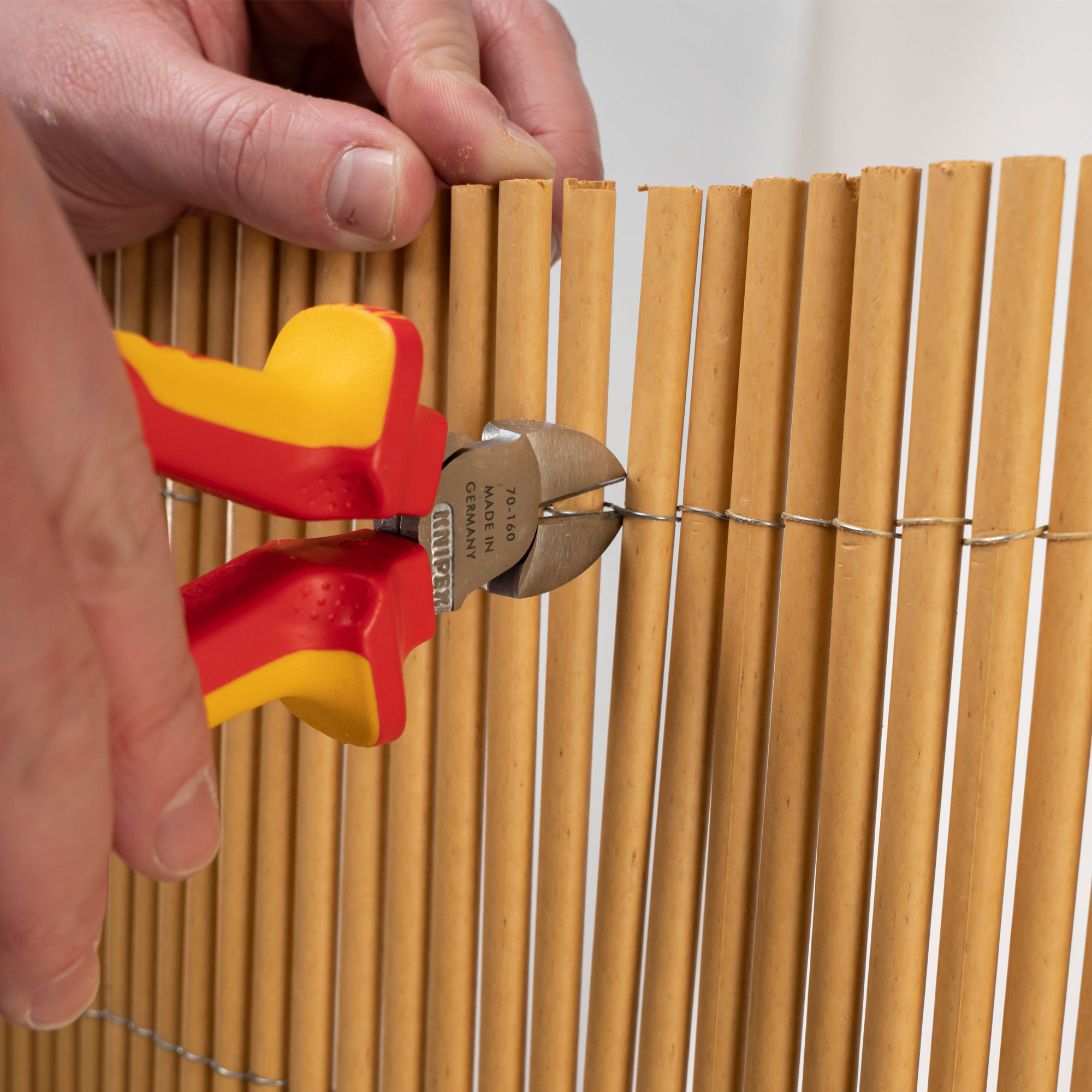 Hand hält Zange, schneidet Draht an Bambusmatte