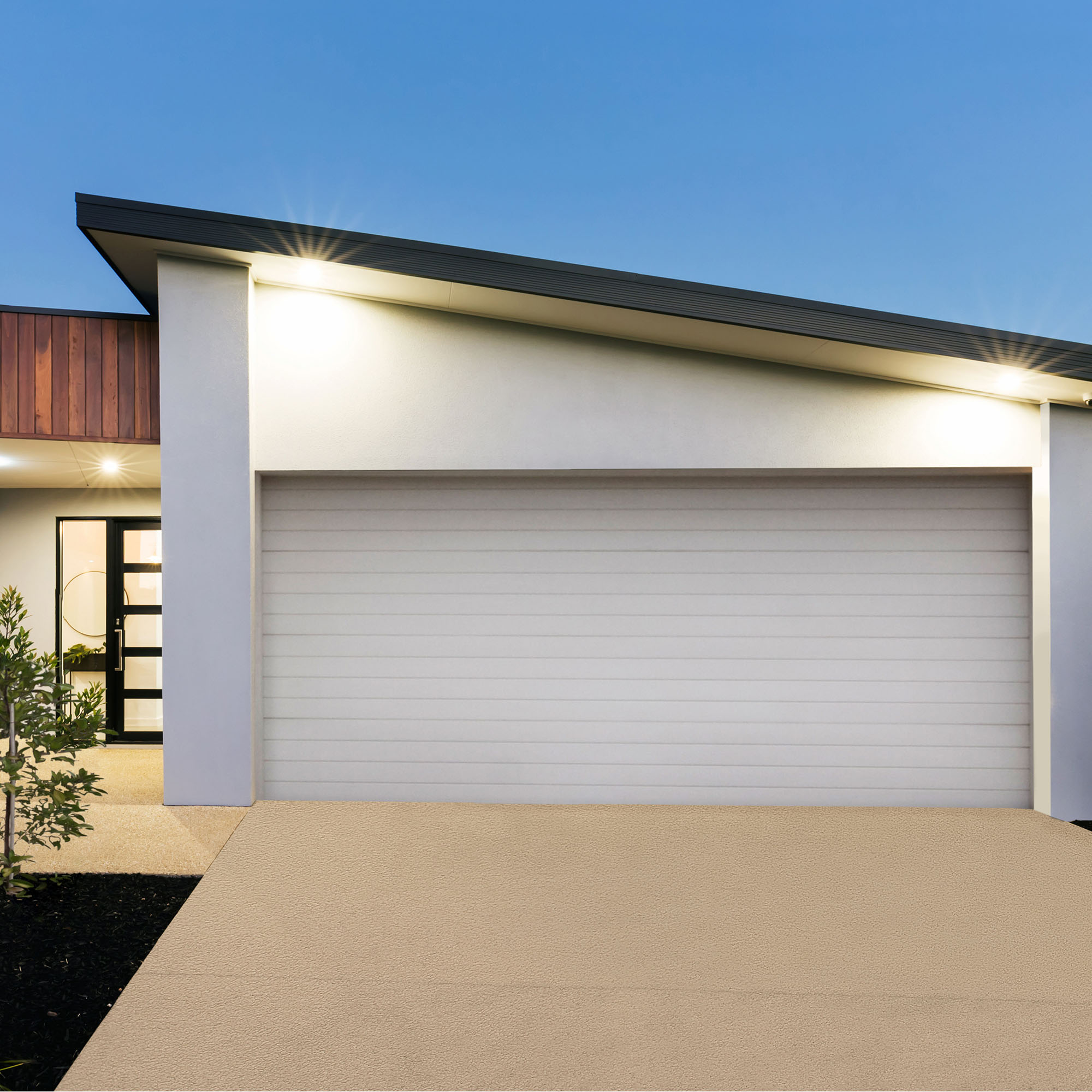 Ein modernes Haus mit geschlossener Garage und beleuchtetem Eingang bei Dämmerung