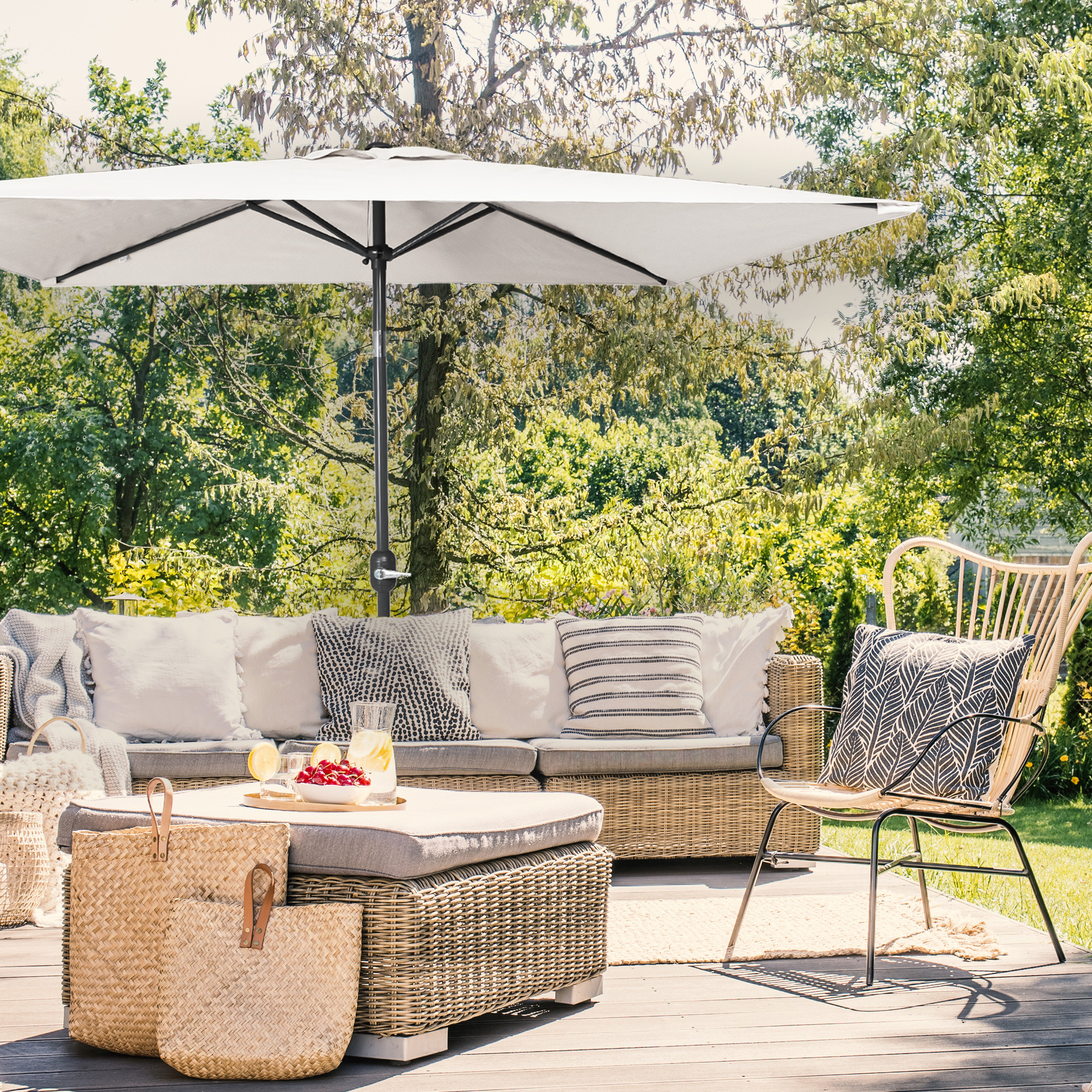 Kleiner, knickbarer Sonnenschirm über einer Terrasse mit Sitzmöbeln und Pflanzen im Hintergrund