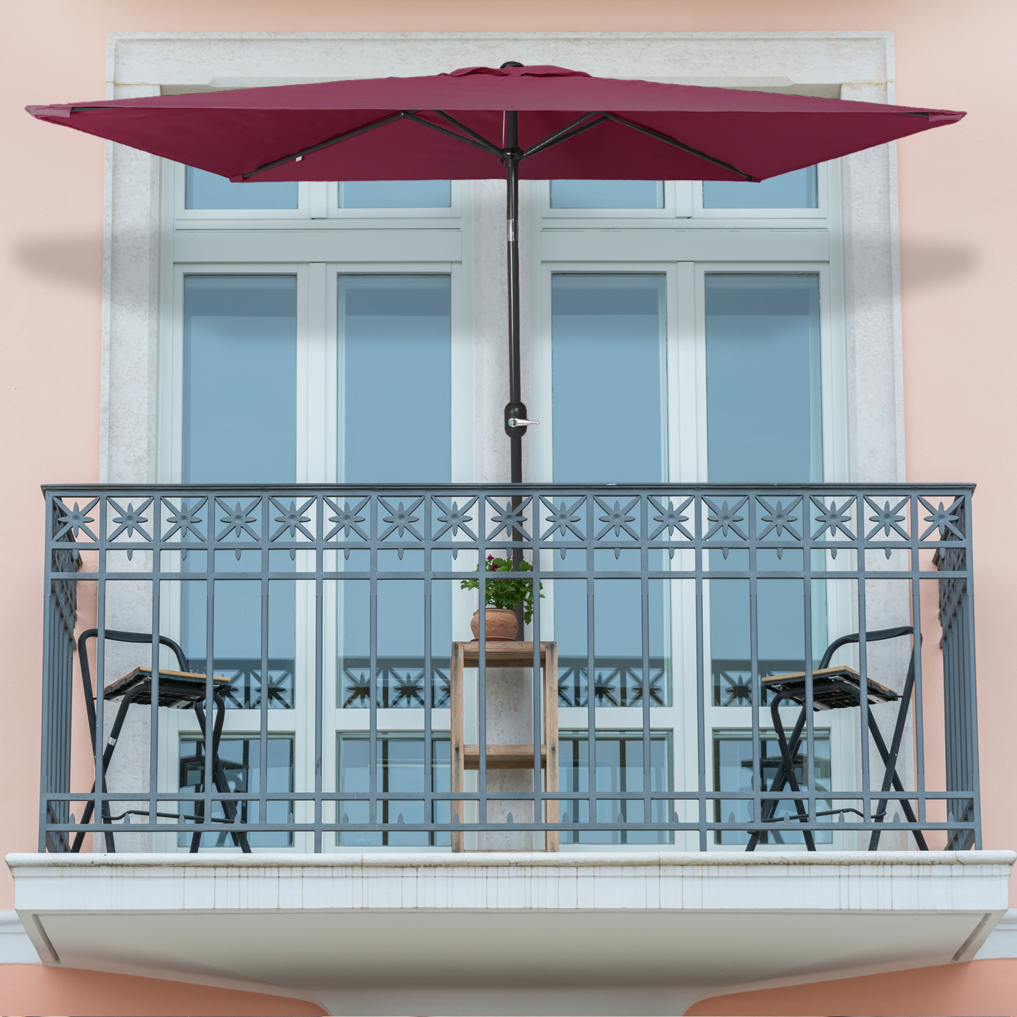 Kleiner, knickbarer Sonnenschirm auf einem Balkon über Tisch und Stühlen