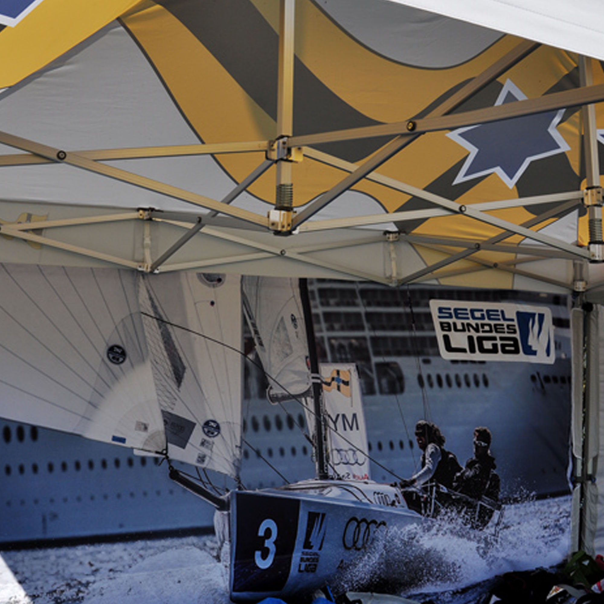 slider_image_01910877d14c78deb7a9fe312674fd7d Gestell eines Faltpavillons mit Segelmotiv und Segel Bundesliga Logo im Hintergrund