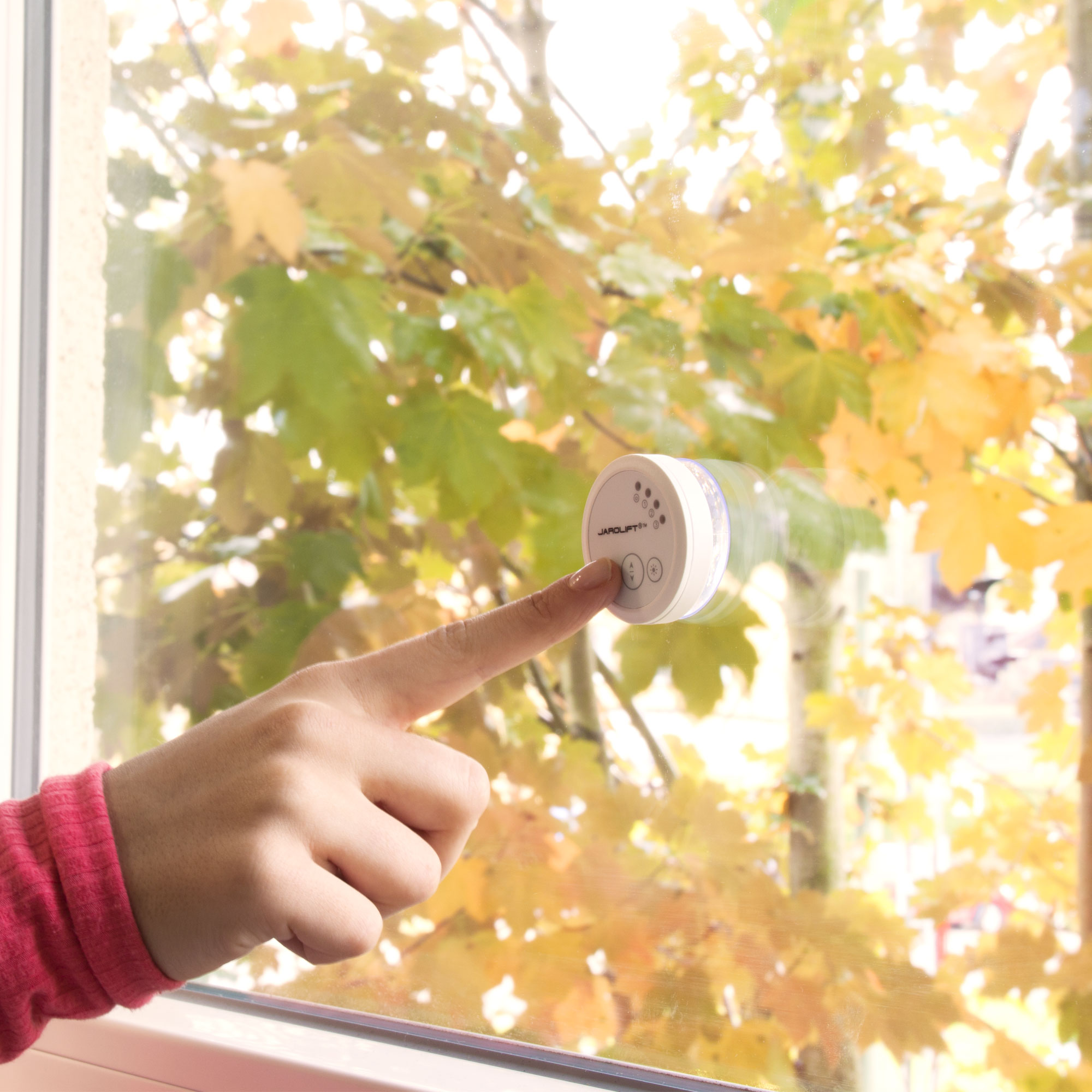 Finger zeigt auf runden Funk Sonnensensor an einem Fenster mit herbstlichem Hintergrund