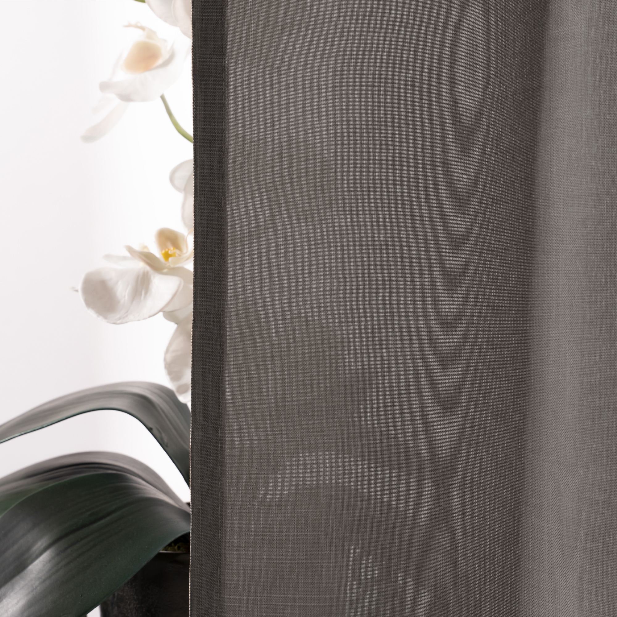 Vorhangdetail mit transparentem Stoff, im Hintergrund eine Pflanze mit Blüten
